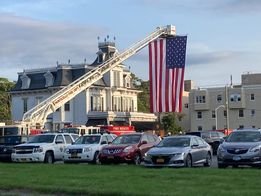Lumberland Engine 21-11 is parked under a flag draped from a Monticello hook-and-ladder truck at an event where firefighters gathered with family and friends to honor Roger Bisland of Glen Spey.